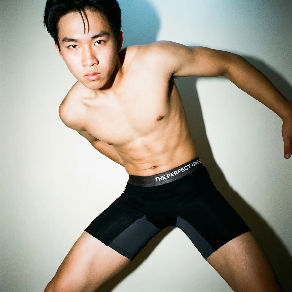 The Perfect Underwear bamboo boxer briefs in black, shown worn on a male model in a studio setting with a close-up view highlighting the waistband and fit.